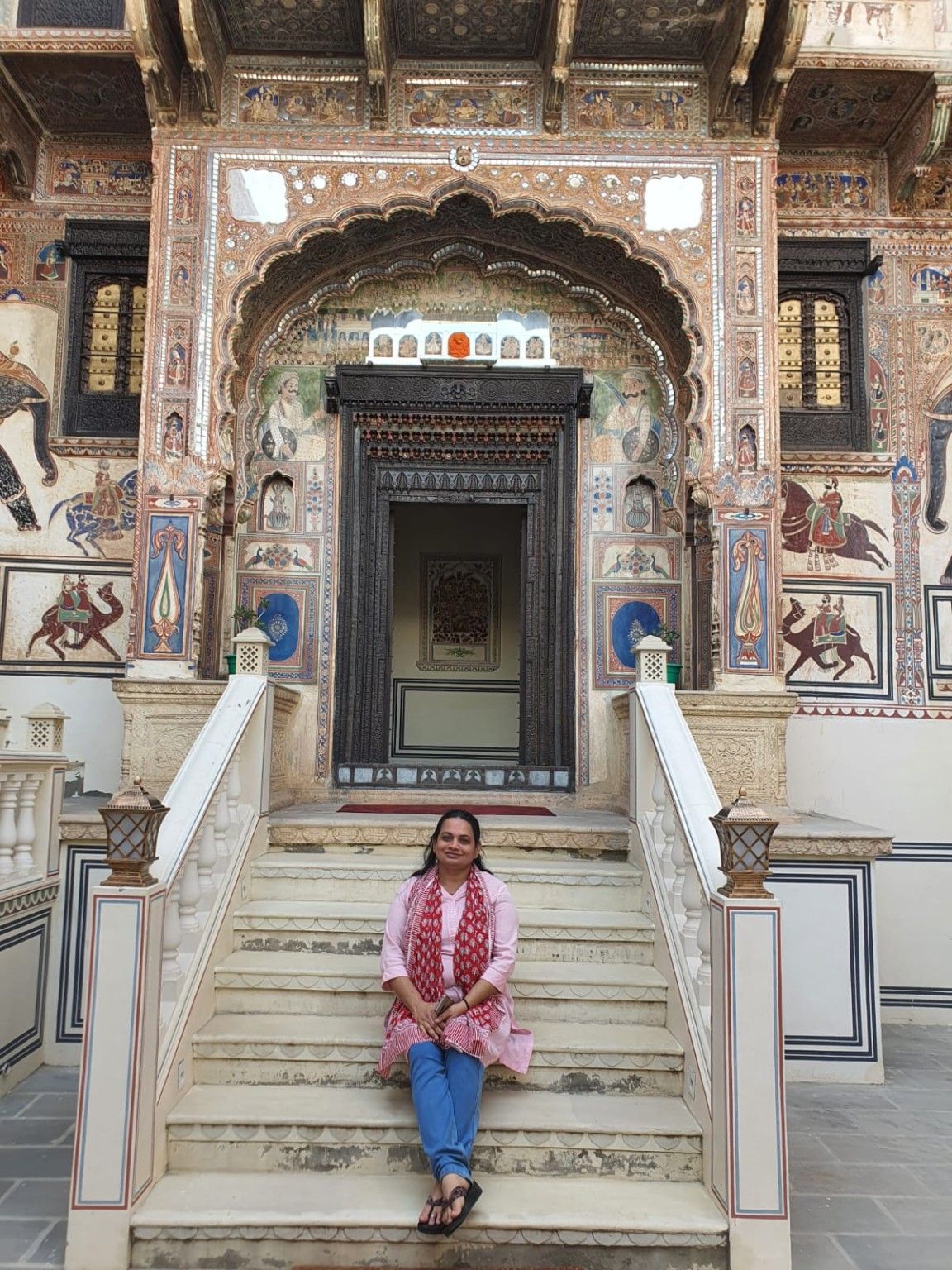 Seated on the steps below a frescoed arched doorway in a Mandawa haveli