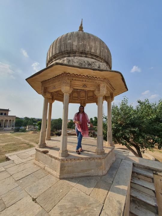 Kalyani standing in a domed stone chhatri under a blue sky